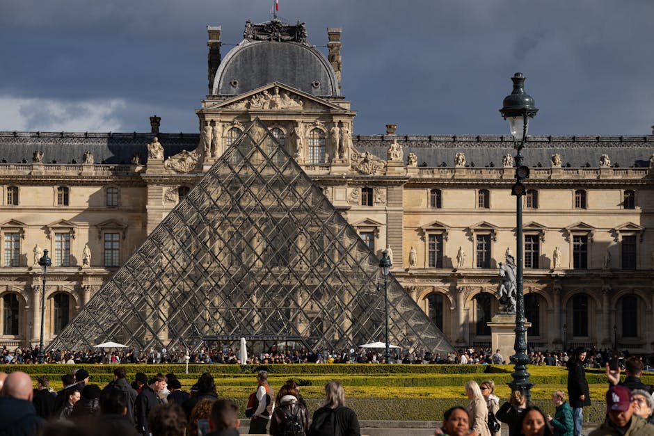 Busy day at the iconic Louvre Pyramid with a crowd of tourists.